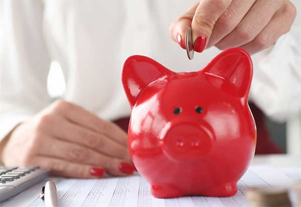 Eine Frau wirft Geld in ein rotes Porzellansparschwein